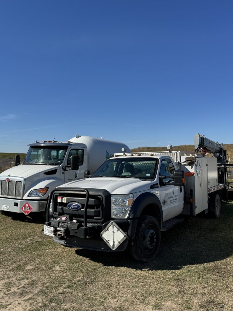 A Noremac Propane service truck equipped with a crane alongside a bobtail delivery truck. This professional fleet is used to handle propane tank installations and fuel deliveries for residential and commercial customers.